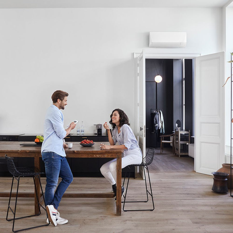 Daikin Sensira binnenunit hoog aan de muur, met twee mensen aan tafel